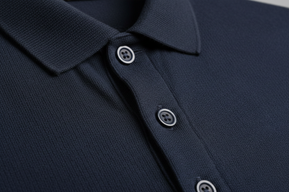 Extreme macro photography of a color: R27 G25 B38 long-sleeve polo shirt. Detailed close-up on the 100% cotton piqué honeycomb texture and the ribbed collar. Focus on the three-button placket with high-quality tonal buttons and precise double-stitching. Soft side-lighting to emphasize the fabric's grain, depth, and premium quality. Clean, professional studio shot, 8k resolution, hyper-realistic.