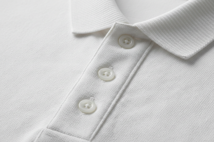 Extreme macro photography of a white long-sleeve polo shirt. Detailed close-up on the 100% cotton piqué honeycomb texture and the ribbed collar. Focus on the three-button placket with high-quality tonal buttons and precise double-stitching. Soft side-lighting to emphasize the fabric's grain, depth, and premium quality. Clean, professional studio shot, 8k resolution, hyper-realistic.