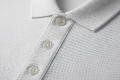 Extreme macro photography of a White short-sleeve polo shirt. Detailed close-up on the 100% cotton piqué honeycomb texture and the ribbed collar. Focus on the three-button placket with high-quality tonal buttons and precise double-stitching. Soft side-lighting to emphasize the fabric's grain, depth, and premium quality. Clean, professional studio shot, 8k resolution, hyper-realistic.